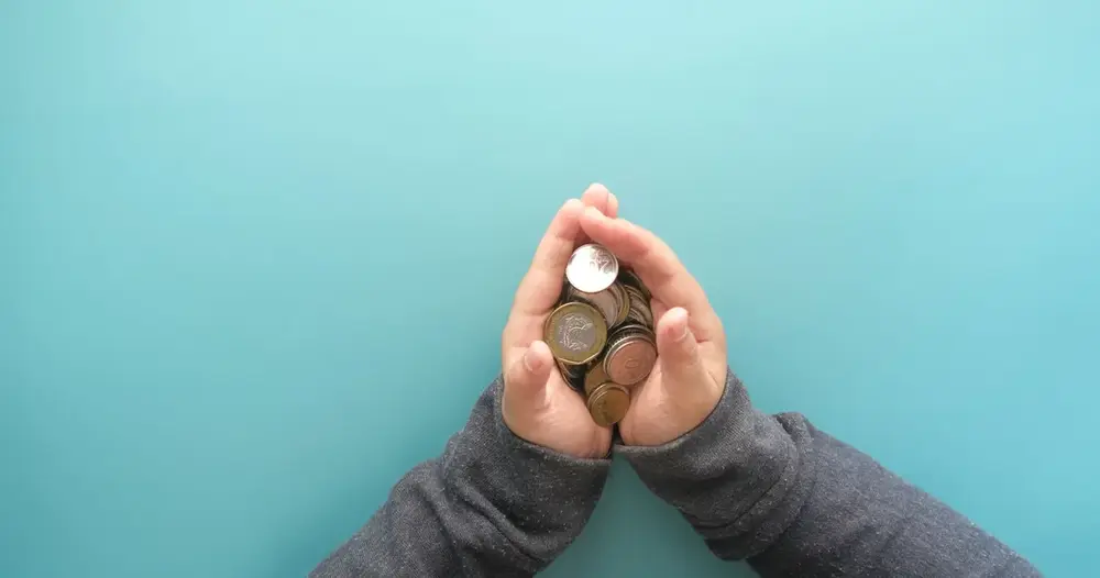 Mãos em concha segurando moedas sobre fundo azul, ilustrando o BPC para idoso e a renda por pessoa da família