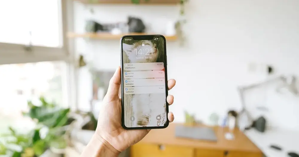 Mão segurando um celular com notificações na tela dentro de casa