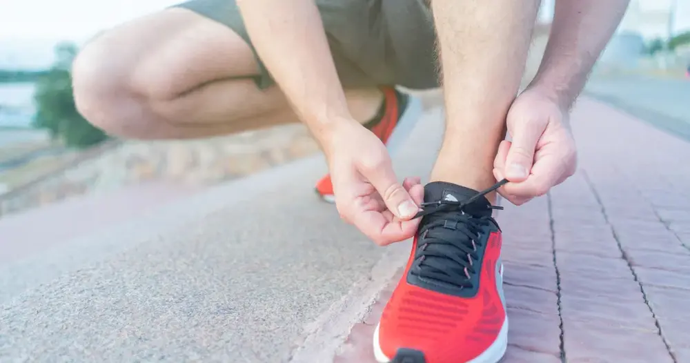 Pessoa amarrando tênis de corrida vermelho em uma calçada, imagem para sites para achar personal trainer em Aparecida de Goiânia
